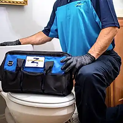 Kneeling Z PLUMBERS service technician with tool bag resting on toilet