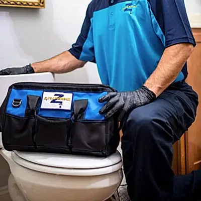 Kneeling Z PLUMBERS service technician with tool bag resting on toilet