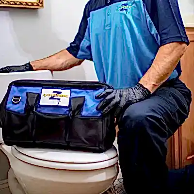 Kneeling Z PLUMBERS service technician with tool bag resting on toilet