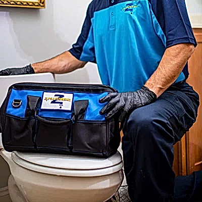 Kneeling Z PLUMBERS service technician with tool bag resting on toilet