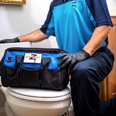 Kneeling Z PLUMBERS service technician with tool bag resting on toilet
